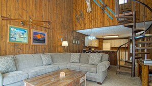 Un interior de madera con un sofá seccional, una mesa de centro, una escalera y una zona de cocina.