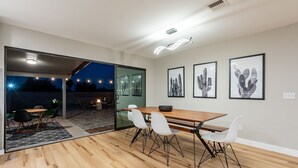 A modern dining area with a wooden table and white chairs, a glass door leading to an outdoor patio, and framed artwork on the wall. - Beautiful Three Bedroom in the Center of Phoenix (Phoenix)