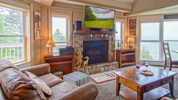 A cozy living room with a stone fireplace, a flat-screen TV mounted above it, leather sofas, and a wooden coffee table.