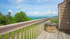A wooden deck with a stone fire pit and a view of green mountains.