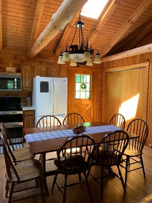 Interior de una cabaña de madera con una mesa de comedor, sillas, un refrigerador, un microondas y una estufa.