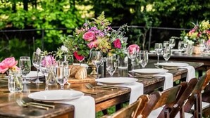 Una larga mesa de comedor al aire libre con varias sillas, cada una con mantel blanco y copas.