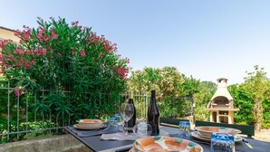 Un espace de restauration en plein air avec une table dressée pour quatre personnes, entouré d’une végétation luxuriante et agrémenté d’une structure décorative en pierre.