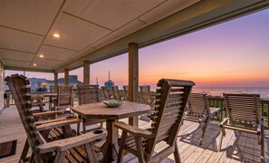 Terraza de madera con asientos exteriores, con vista a una puesta de sol sobre el océano.