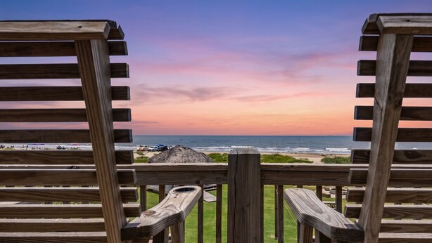 A wooden deck with a view of the ocean and beach at sunset. - Beachfront | Firepit, Volleyball & Gazebo Dining (Port Bolivar)