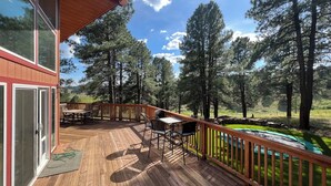 A wooden deck with outdoor furniture, a stone wall, and a view of a forest. - Secluded Mountain Home in the Pines (Flagstaff)