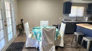 A compact kitchen with a dining area, featuring a table set with chairs, a sink, and a window with blinds. - Roadrunner Bedroom in La Quinta Cove (La Quinta)
