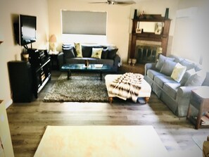 Ett vardagsrum med en soffa, en pall, ett soffbord och en tv.