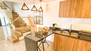 Una cucina moderna con mobili in legno, un piano di lavoro nero e un'isola integrata. Una scala conduce a un altro livello e lampade a sospensione illuminano l'isola.