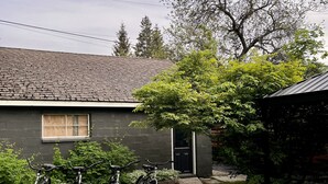 Une maison à l’extérieur d’un gris foncé, avec un toit en tuiles et un petit jardin devant, où sont garés trois vélos.