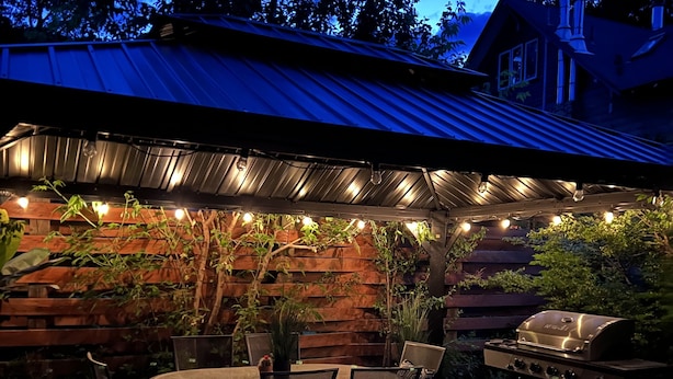Une terrasse extérieure avec une table et des chaises, un barbecue et des guirlandes lumineuses.