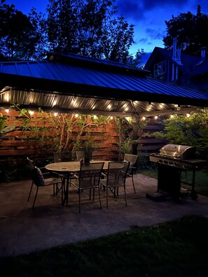 Une terrasse extérieure avec une table et des chaises, un barbecue et des guirlandes lumineuses.