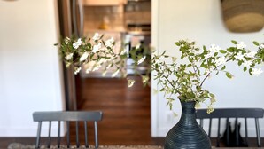Un coin repas avec une table, un vase de fleurs et un saladier de fruits.