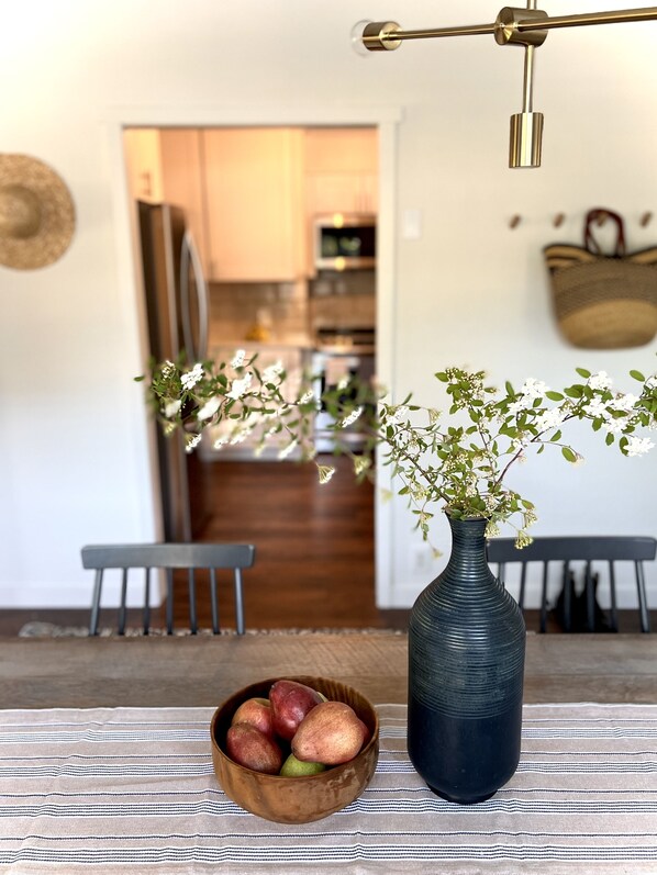 Un coin repas avec une table, un vase de fleurs et un saladier de fruits.