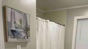 A bathroom with a shower curtain, a towel rack, and a framed picture on the wall. - Dudley's Southern Charm (Bossier City)