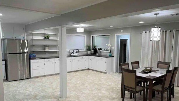A spacious kitchen with white cabinets, a stainless steel refrigerator, and a dining area with a table and chairs. - Dudley's Southern Charm (Bossier City)