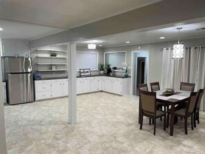 A spacious kitchen with white cabinets, a stainless steel refrigerator, and a dining area with a table and chairs. - Dudley's Southern Charm (Bossier City)