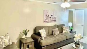 A living room with a sofa, a side table, a ceiling fan, and a painting on the wall. - Dudley's Southern Charm (Bossier City)