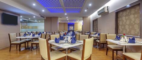 A restaurant with multiple tables and chairs, ceiling lights, and an air conditioning unit.