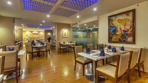 A spacious restaurant with wooden flooring, round tables, and blue napkins. - Golden Tulip New Delhi - Hari Nagar (New Delhi)