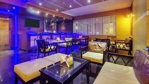 A modern restaurant with a bar area, seating with cushioned chairs and tables, and a large screen on the wall. - Golden Tulip New Delhi - Hari Nagar (New Delhi)