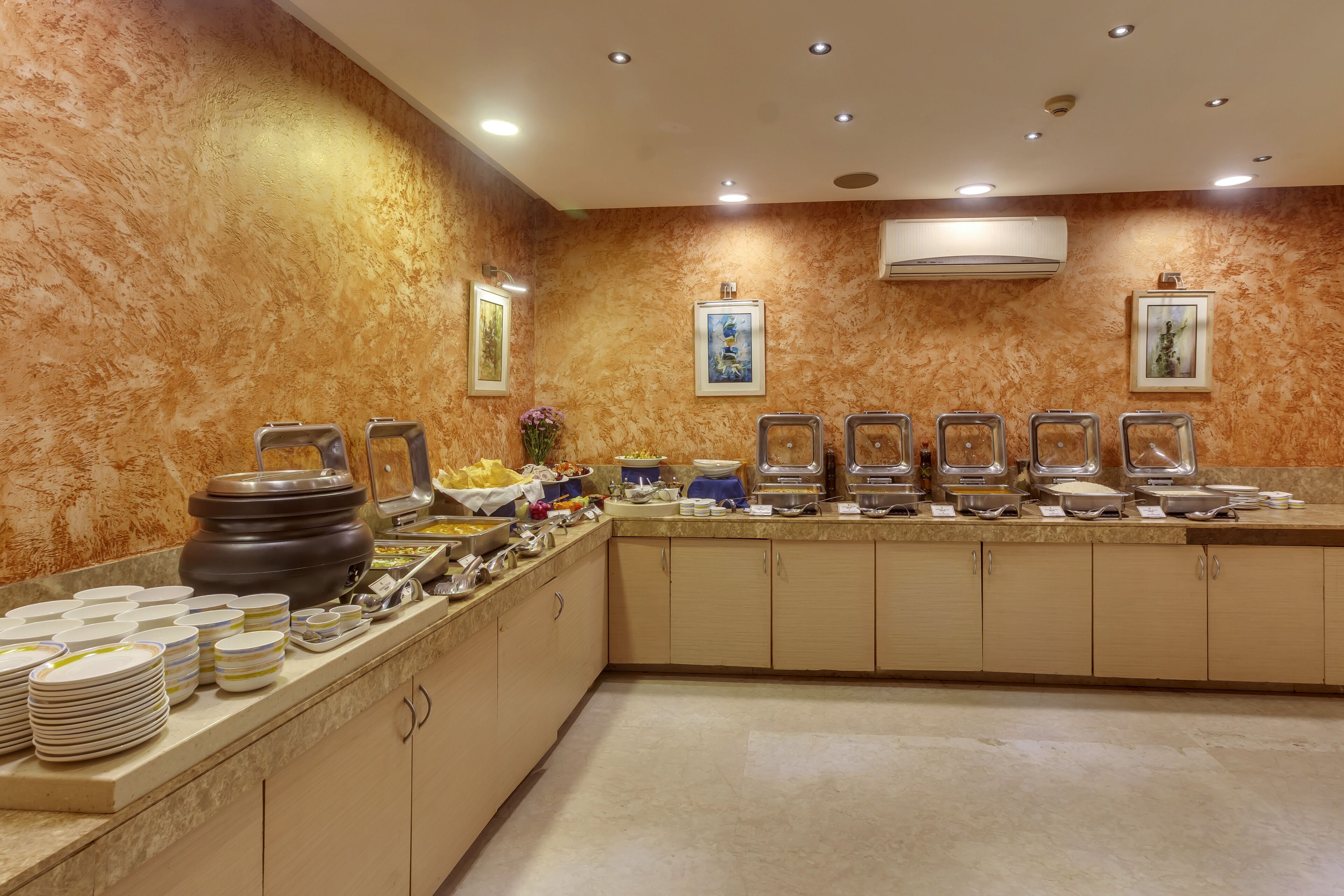 Montaje tipo buffet con varias estaciones de comida, una olla grande y platos apilados sobre una barra.
