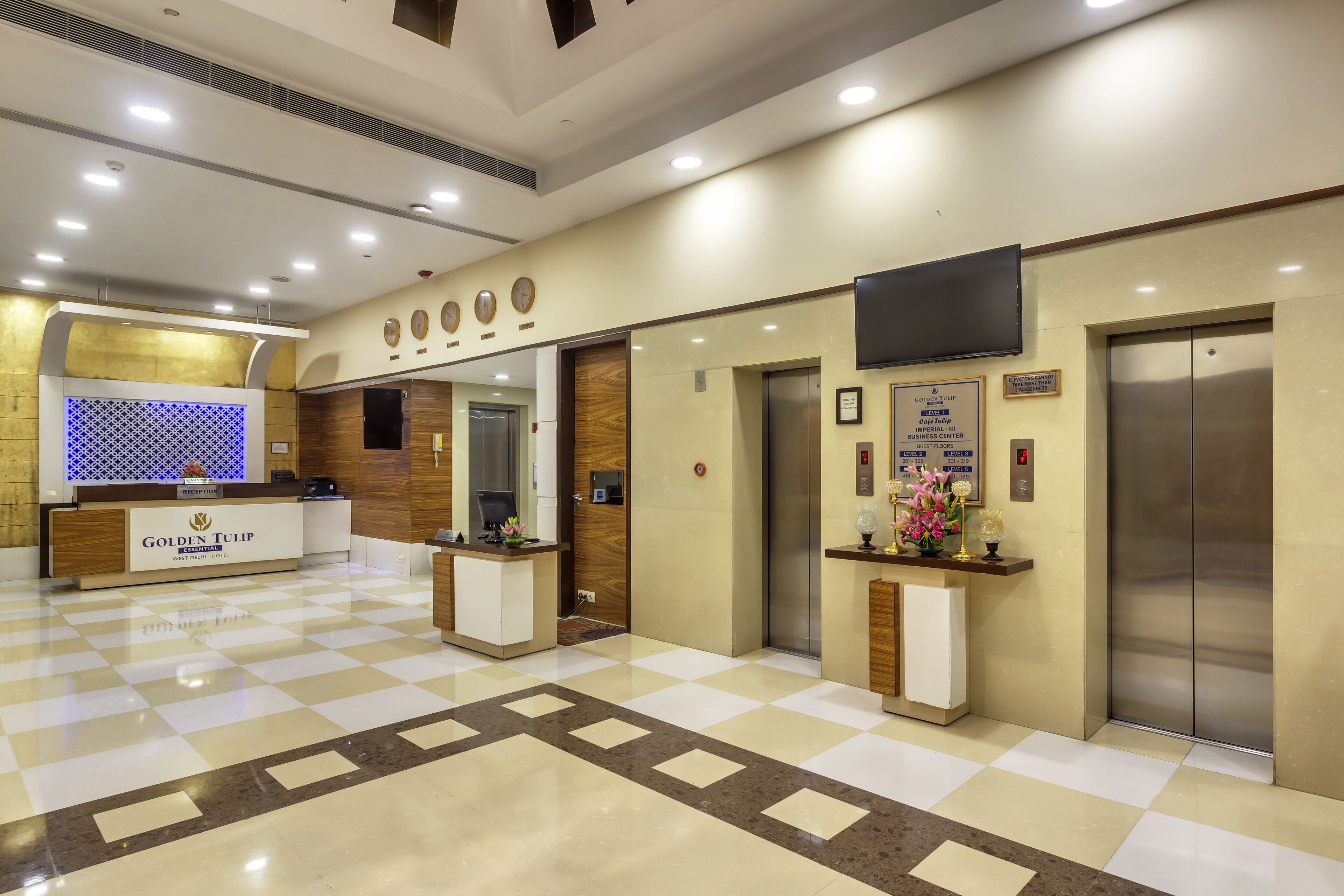 A hotel reception area with a check-in counter, reception desk, and two elevators.