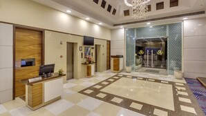 A hotel reception area with a reception desk, a chandelier, and a patterned floor. - Golden Tulip New Delhi - Hari Nagar (New Delhi)