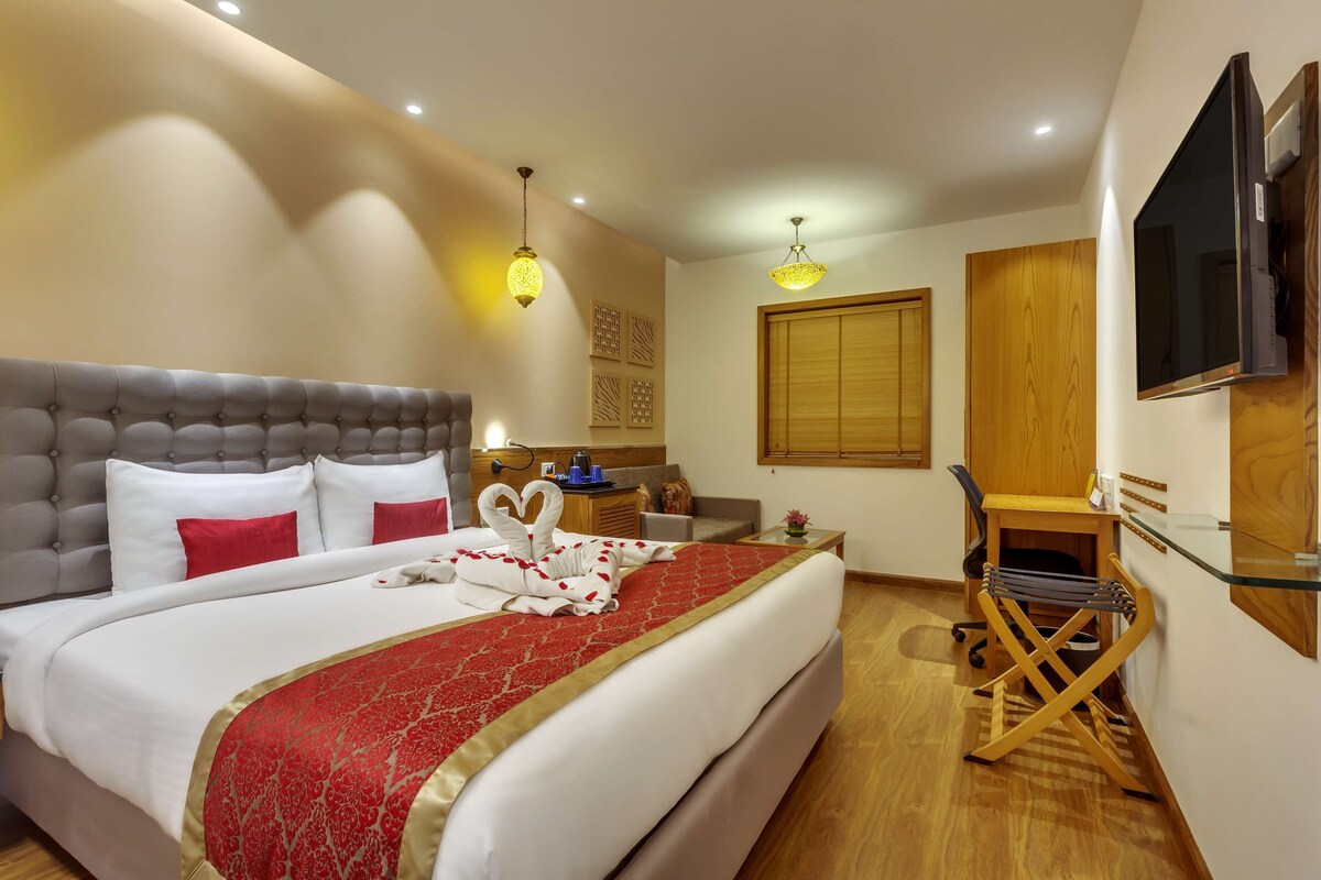 A hotel room with a large bed, a desk, a chair, a TV, and a wooden wardrobe.