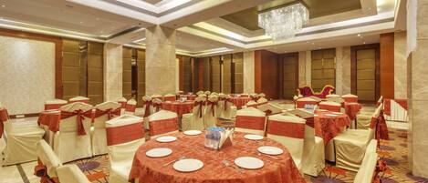Un salón de banquetes con mesas redondas, sillas y una lámpara de araña.