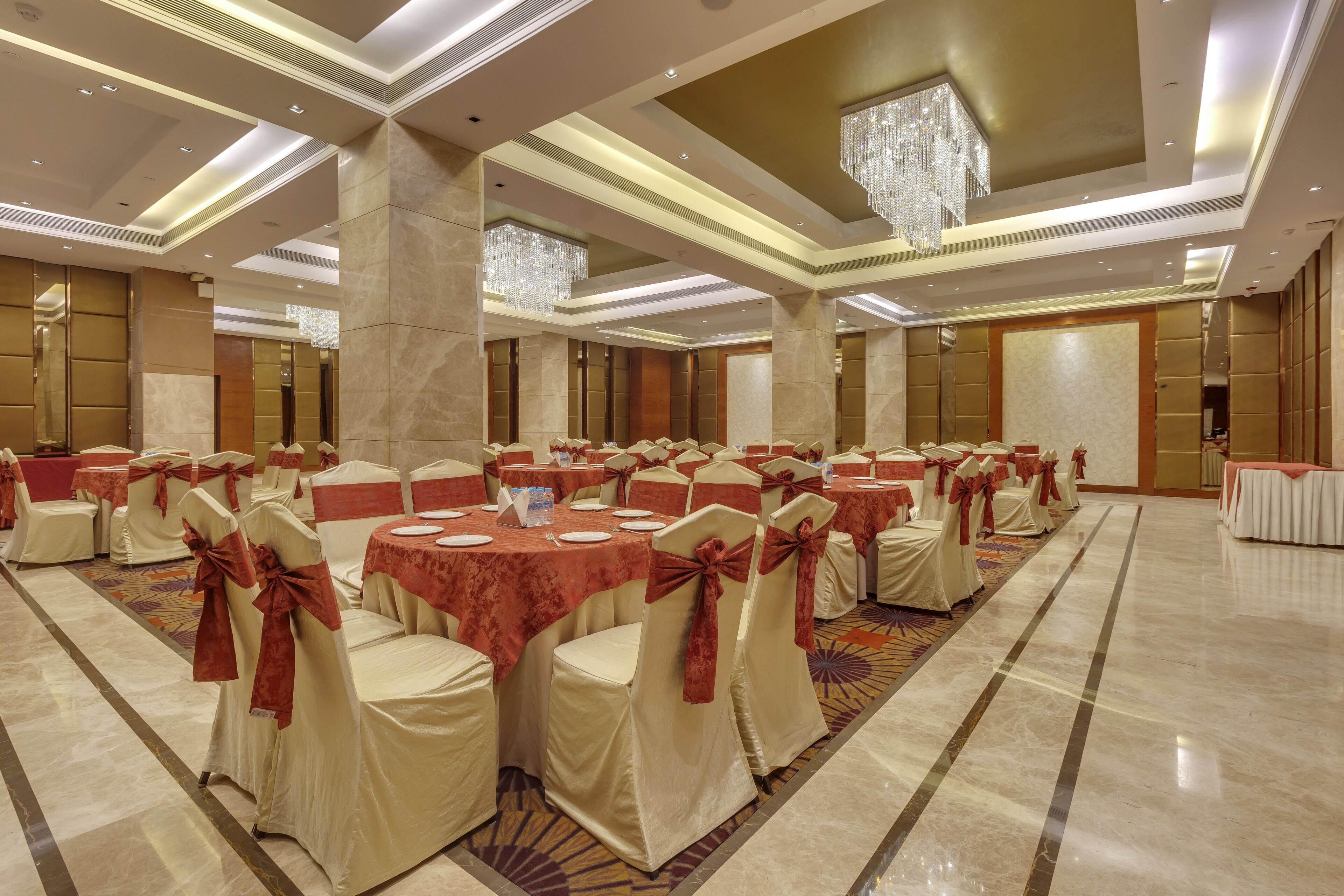 A banquet hall with round tables, chairs with red sashes, and a chandelier.