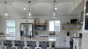Cocina amplia con armarios blancos, una isla central con taburetes y luminarias colgantes.