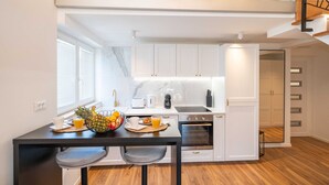 Una cocina moderna con armarios blancos, una mesa de comedor con sillas y una zona de desayuno con frutas y una cafetera.