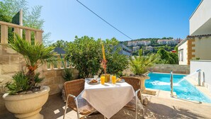 Un patio al aire libre con piscina, mesa de comedor, sillas y plantas en macetas.