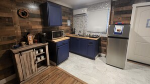 Eine kompakte Küche mit Holzschränken, einer Mikrowelle, einer Kaffeemaschine und einem Edelstahlkühlschrank.