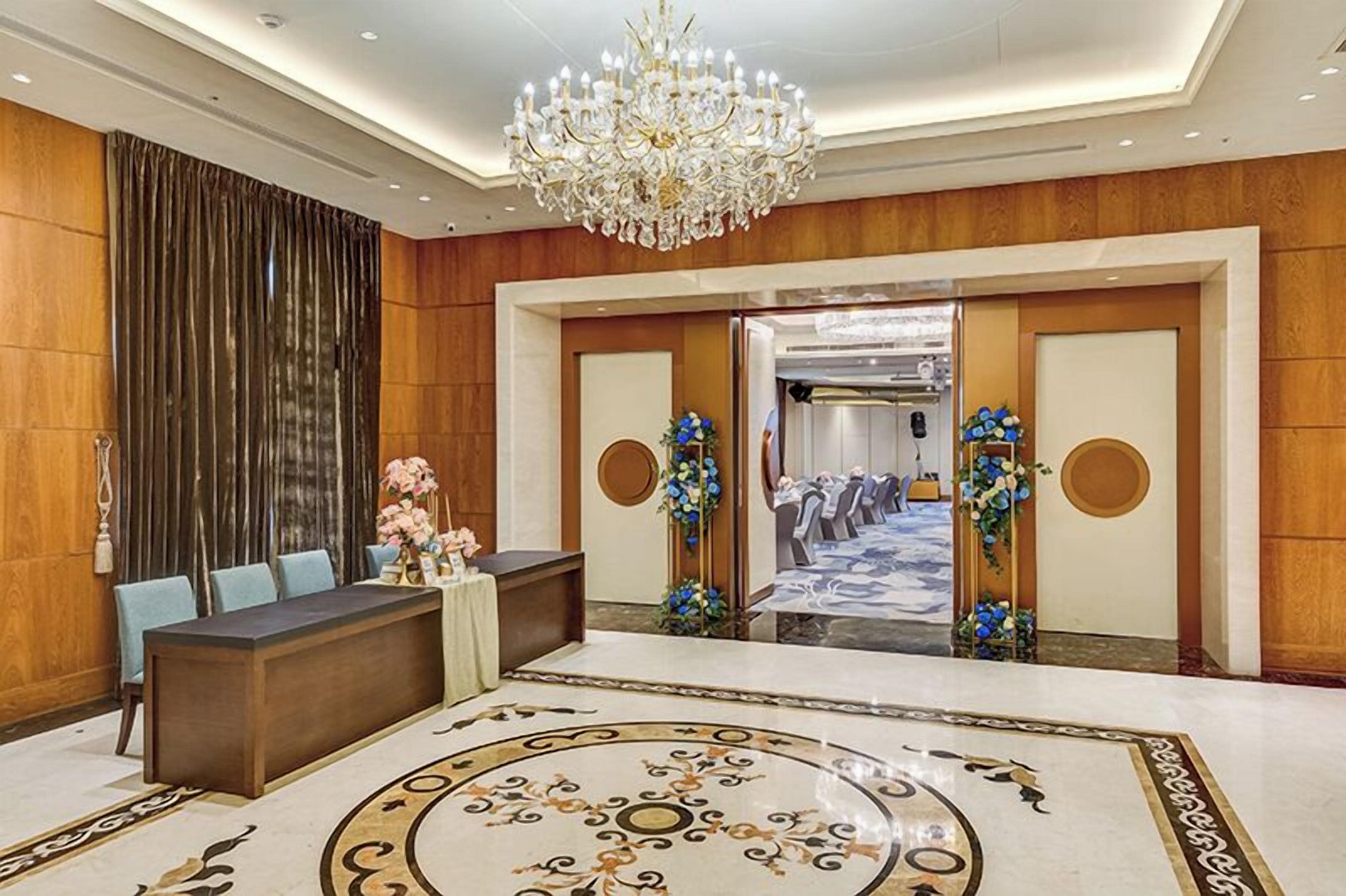 Un vestíbulo de hotel con una recepción, una araña y suelo alfombrado.