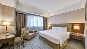 A hotel room with a large bed, a desk, a chair, a nightstand, and a window with curtains.