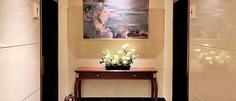 An elevator with a painting on the wall, a small table with flowers, and a fire extinguisher on the floor.