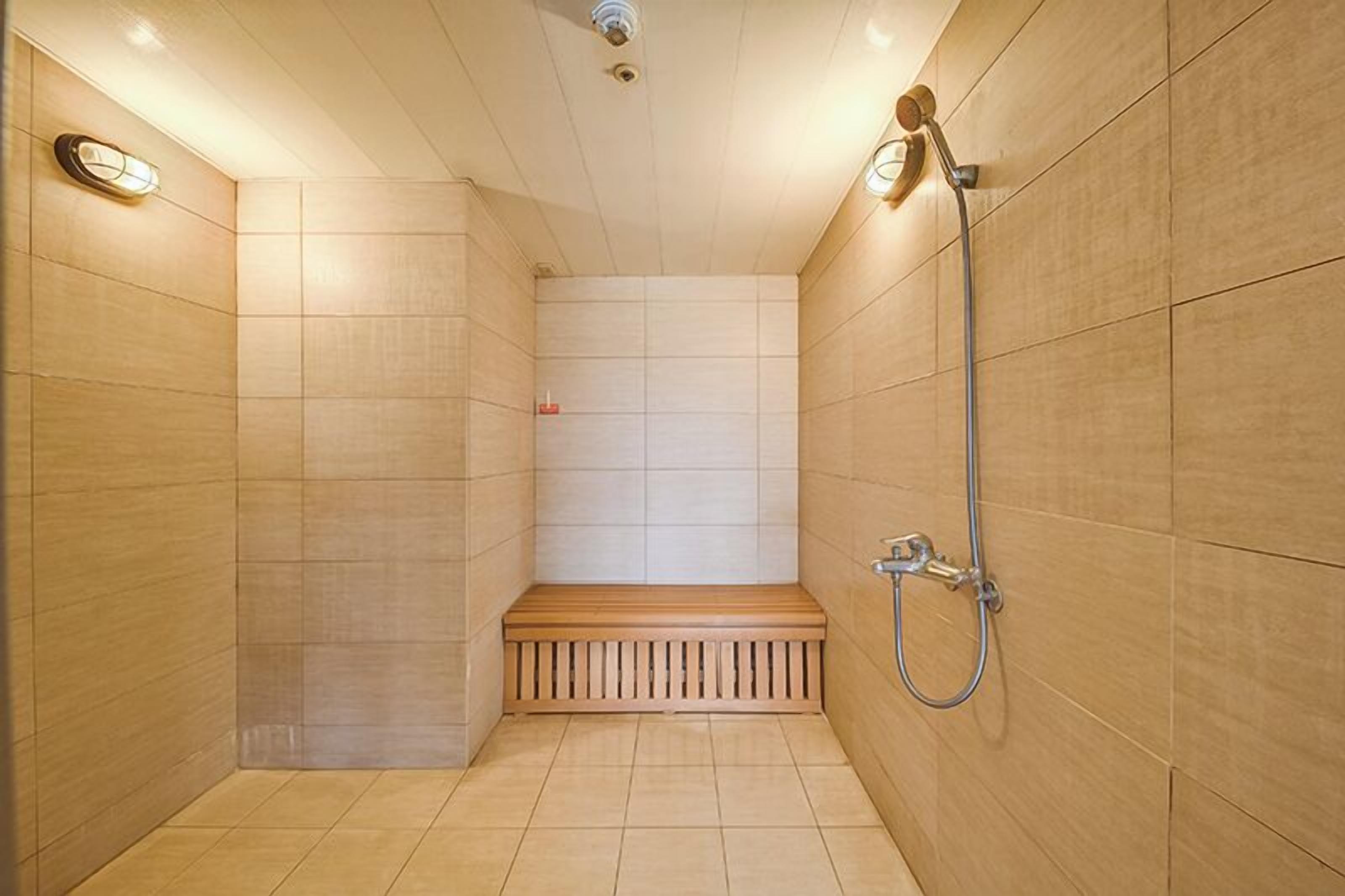 A small, enclosed shower area with tiled walls, a wooden bench, and a handheld showerhead.