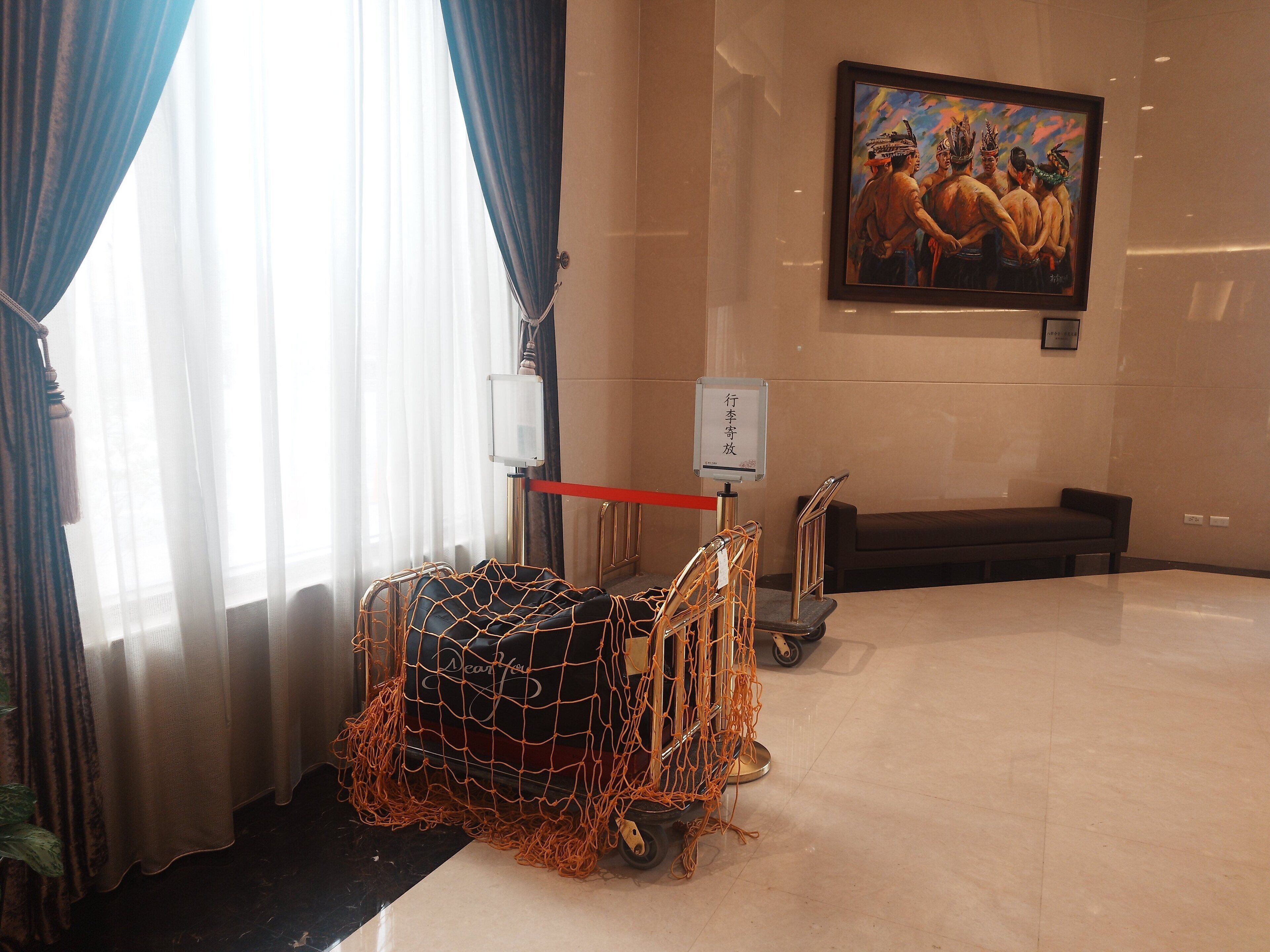 A hotel lobby with a large painting on the wall, a desk, and a cart covered with orange netting.
