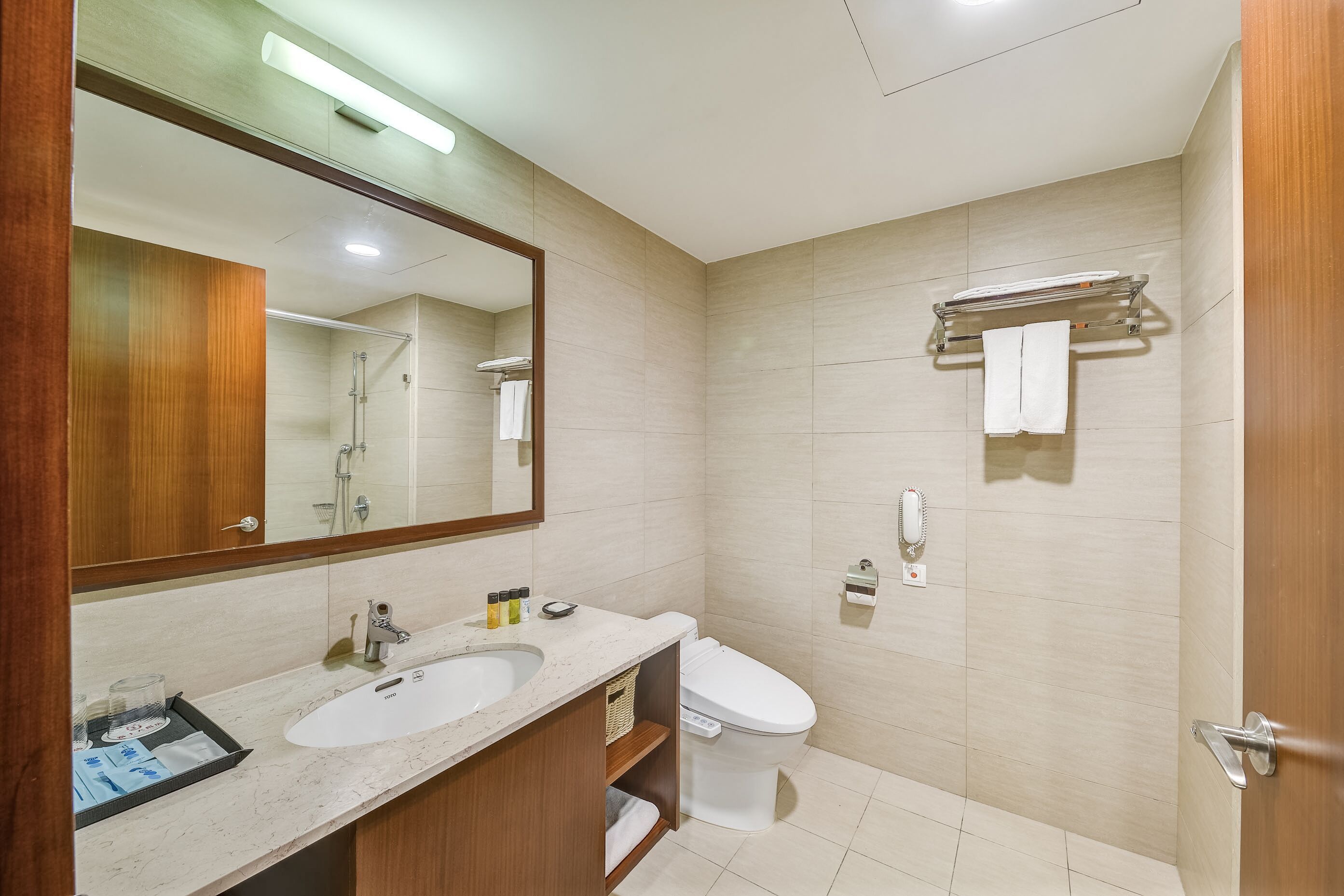 A modern bathroom with a large mirror, two sinks, a toilet, and a shower.