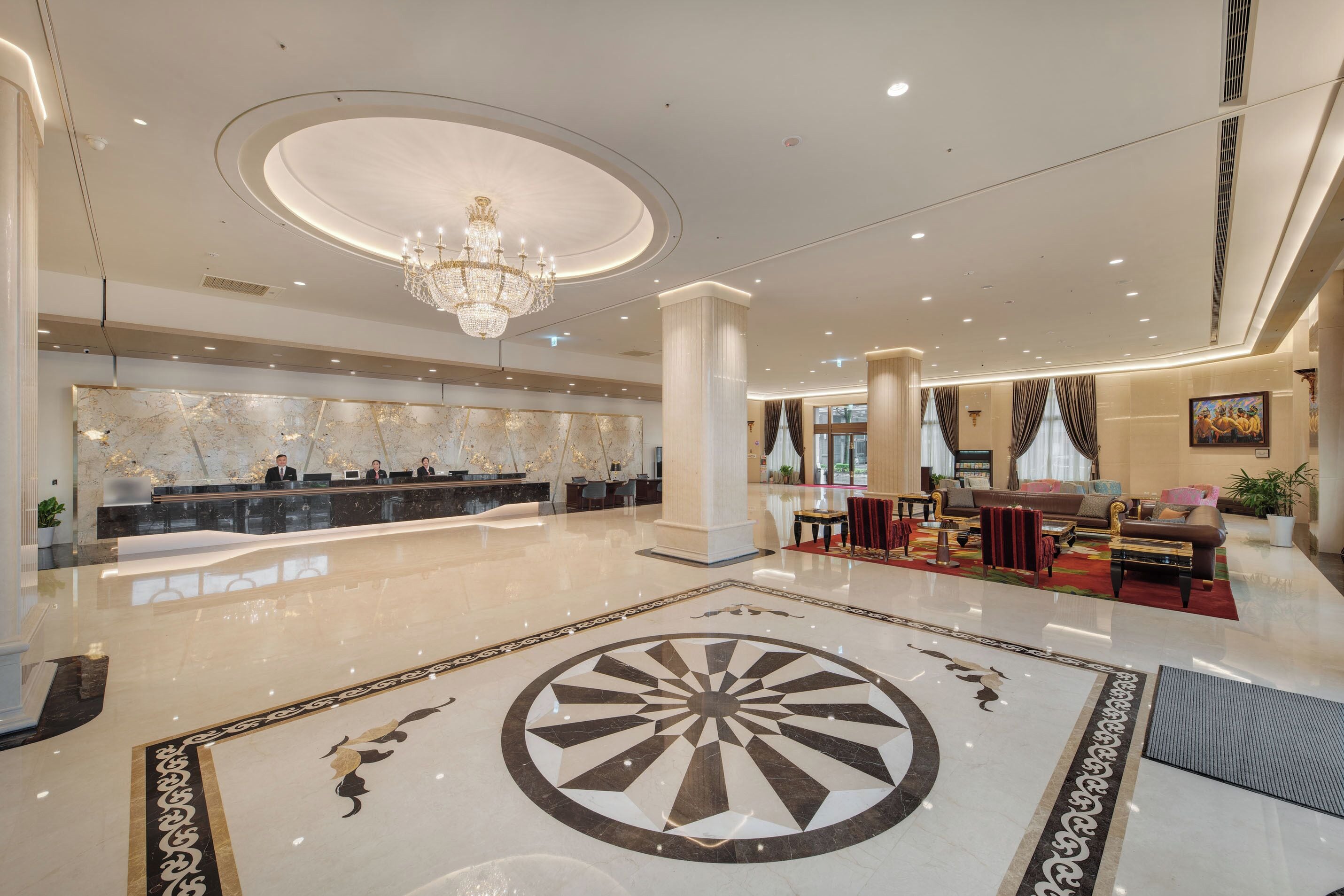 A spacious lobby with a marble reception desk, a chandelier, and a large circular floor design.