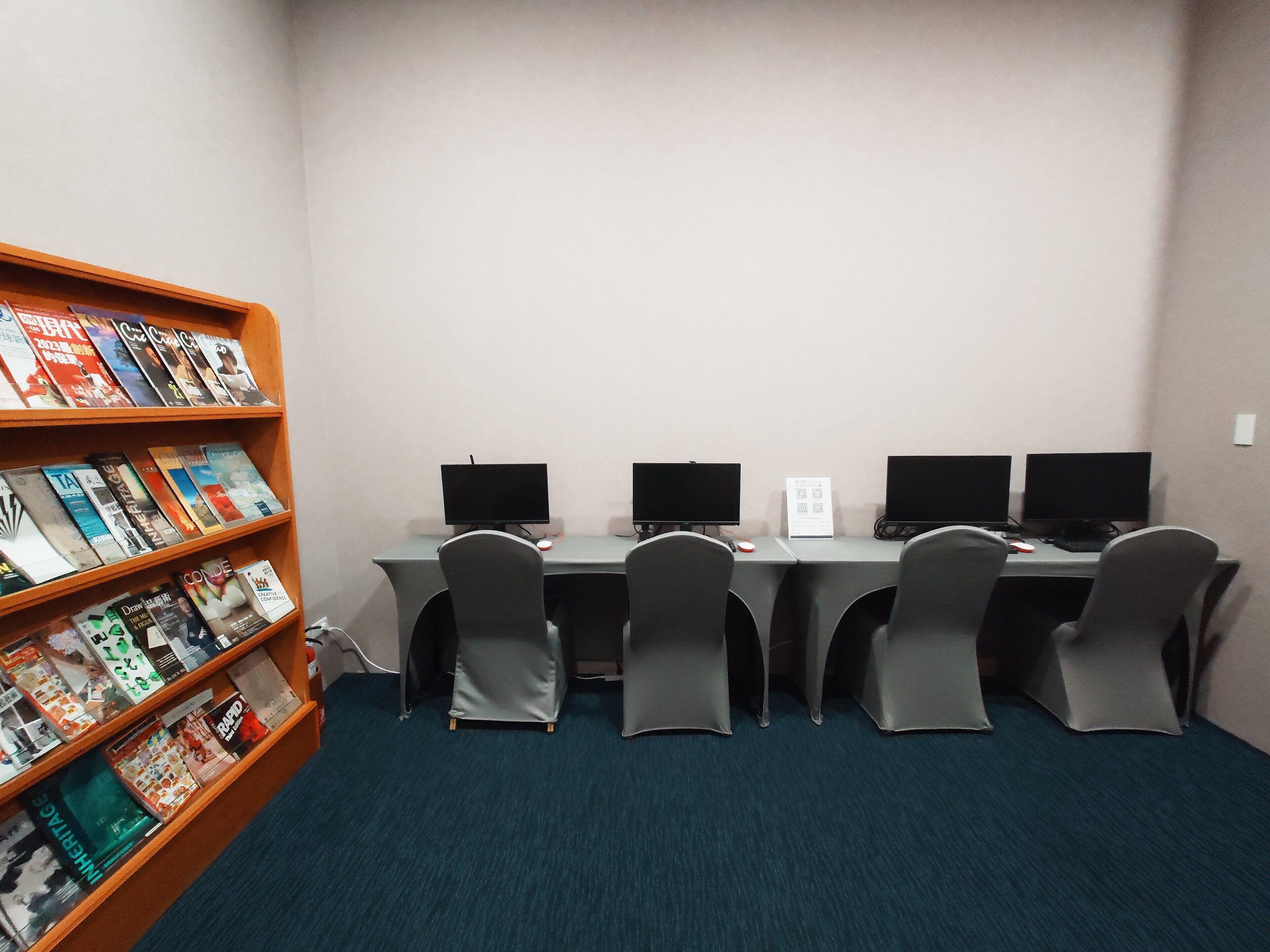A computer lab with four workstations, each with a monitor, keyboard, and mouse. There is a bookshelf filled with books to the left.