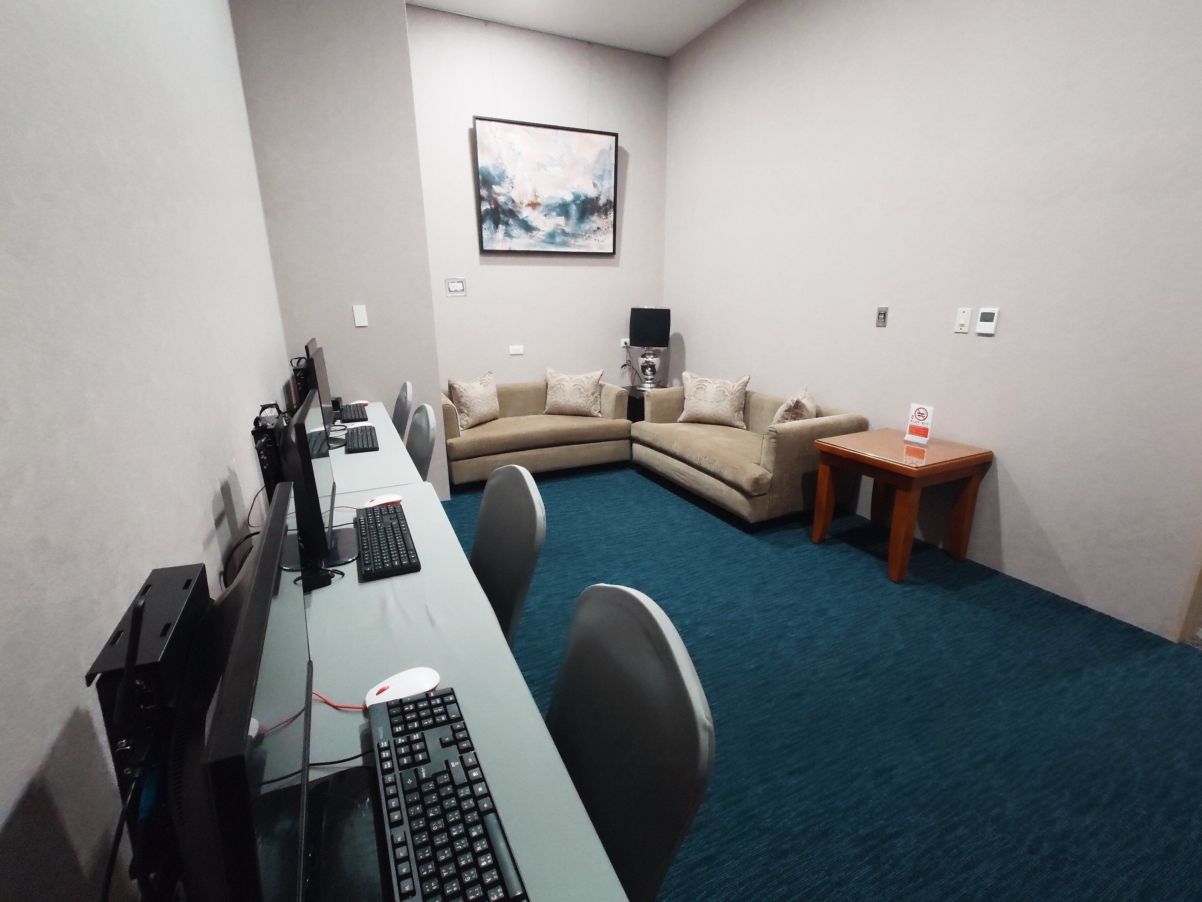 A conference room with a long table, two chairs, a sofa, a small table with a sign, and a painting on the wall.