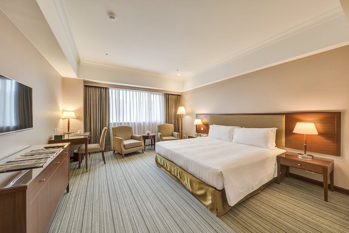 A hotel room with a large bed, a desk, a chair, a TV, and a lamp.