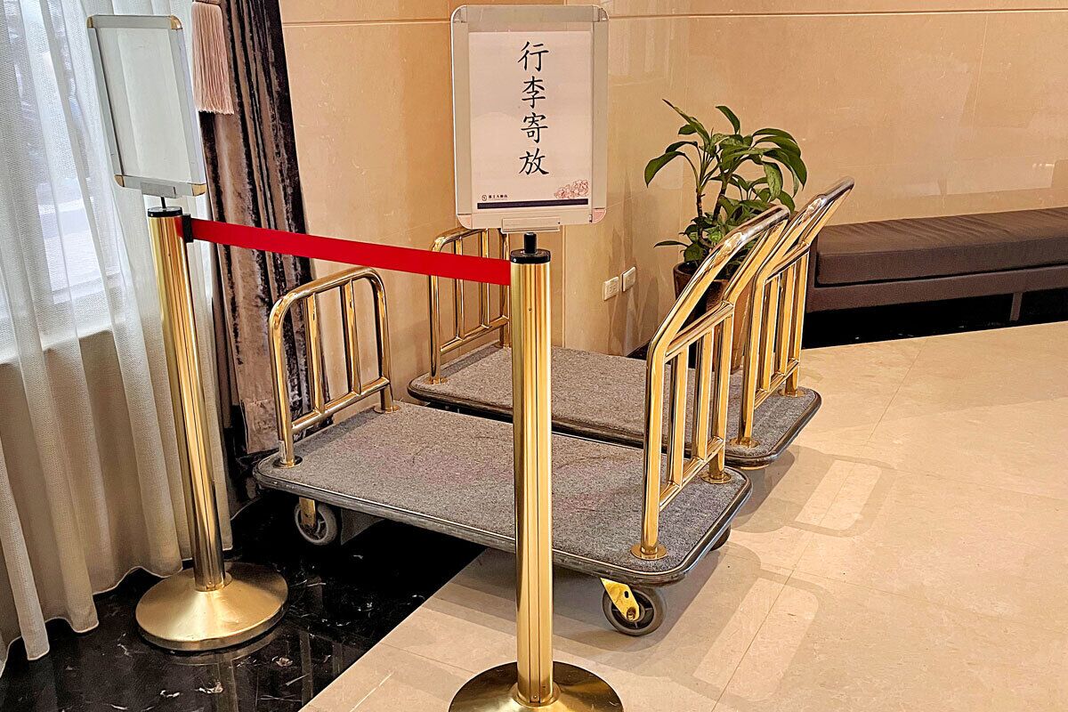 Entrada de un hotel con una barrera roja, un ascensor dorado y un letrero con caracteres chinos.