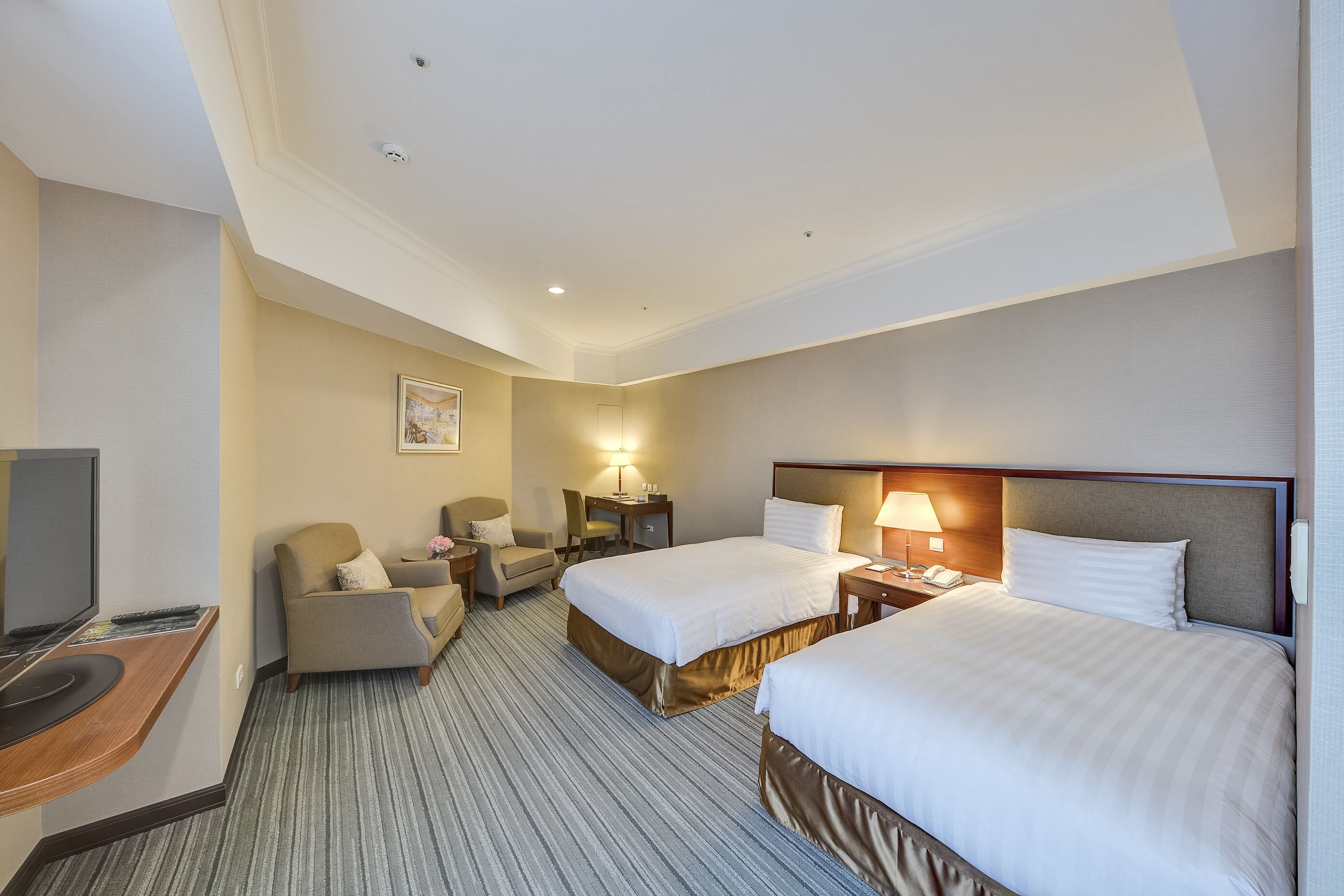 A hotel room with two beds, a desk with a computer, a chair, a TV, and a lamp.