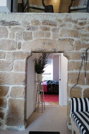 A stone archway labeled "N°10" leading to a room with a red carpet, a potted plant, and a black and white striped sofa. - Casa Alana (Polientes)