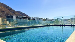 En swimmingpool med kristallklart blått vatten, omgiven av ett glasräcke och en betongplattform.