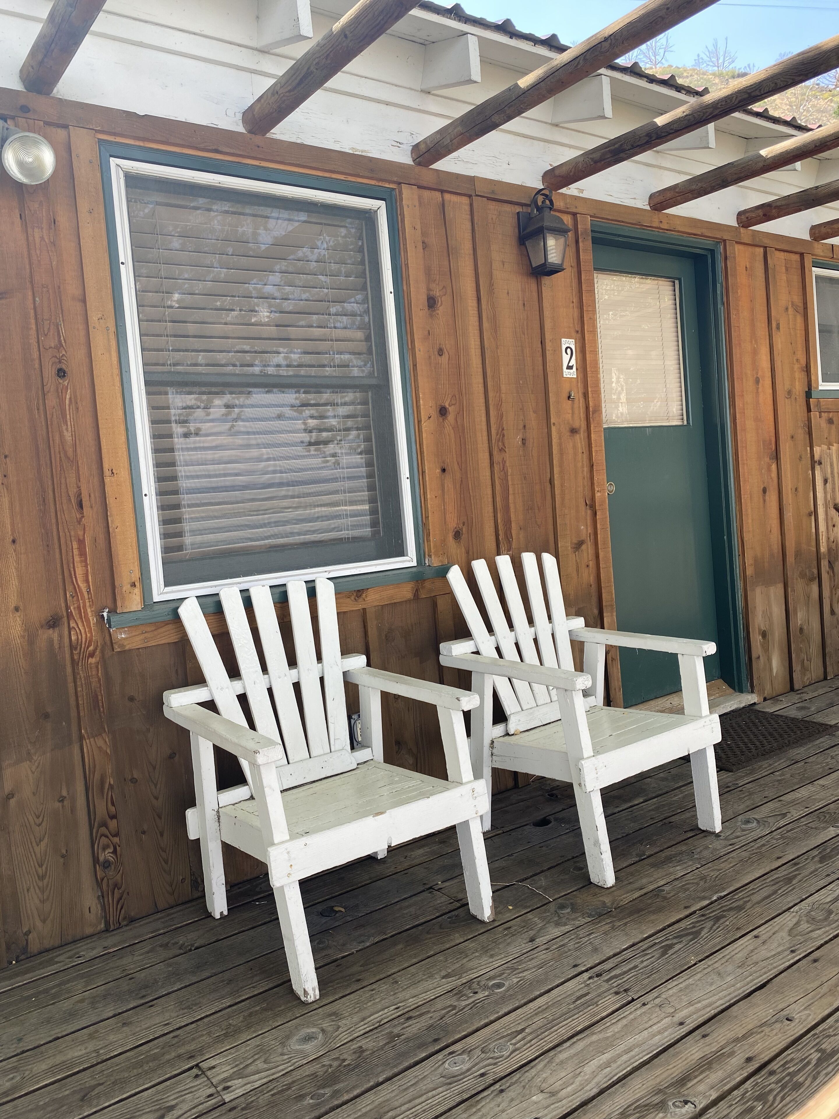 Een houten terras met twee witte Adirondack-stoelen en een groene deur.